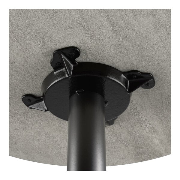 A close-up view of the underside of a round table showing a black cast iron base attached to a gray laminated tabletop.