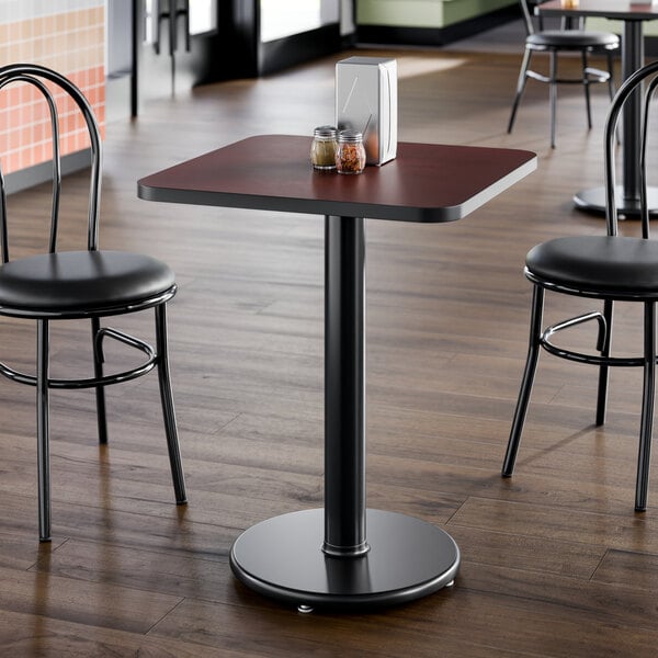 A square, standard height restaurant table with a reversible cherry and black laminated top and a round cast iron base.