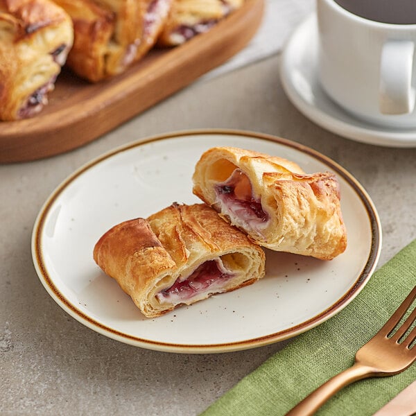 A white plate with two Orange Bakery blueberry cream cheese filled croissants and a cup of coffee on a table.