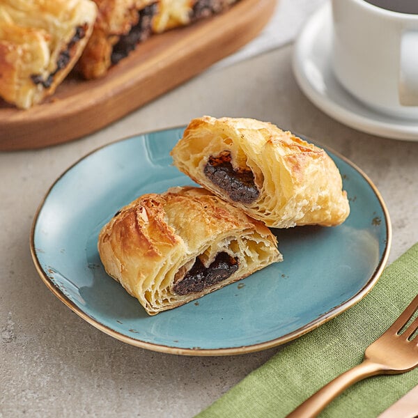 A plate with two Orange Bakery ready to bake chocolate filled croissants and a cup of coffee on a table.