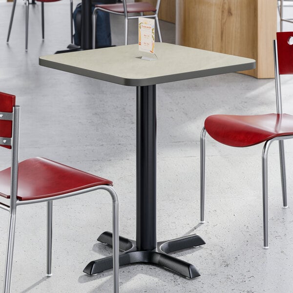 A square reversible gray and white laminated table with a black cast iron base, shown with red chairs in a dining area.