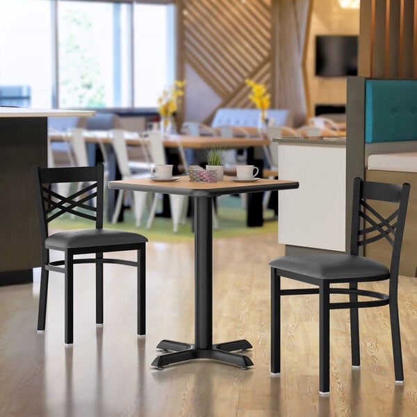 A Lancaster Table & Seating table with a walnut top and oak base next to two black chairs.