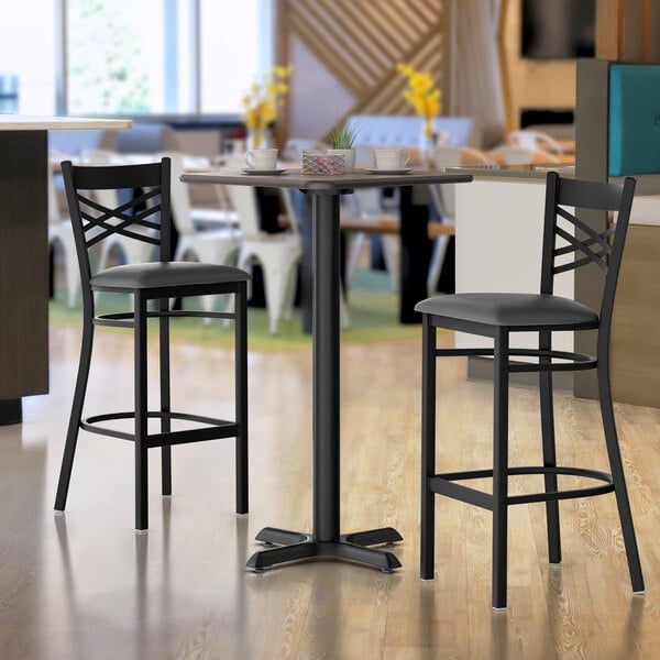 A Lancaster Table & Seating white birch and ash bar height table with a black base and two black chairs.