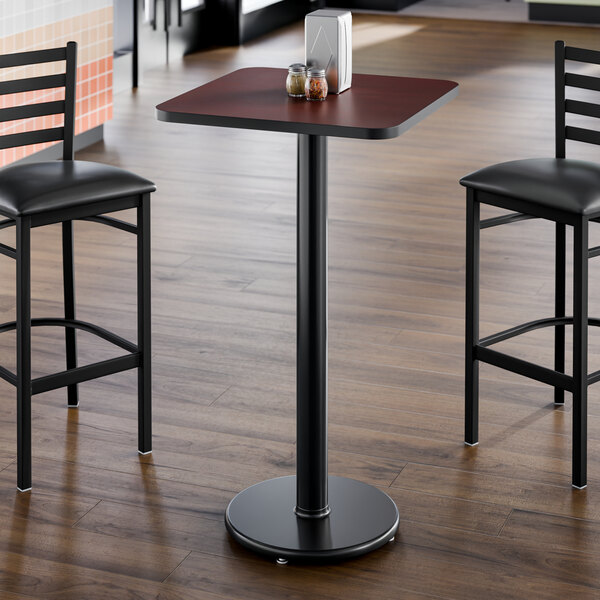 A square bar height table with a reversible cherry and black laminated top and a round cast iron base.