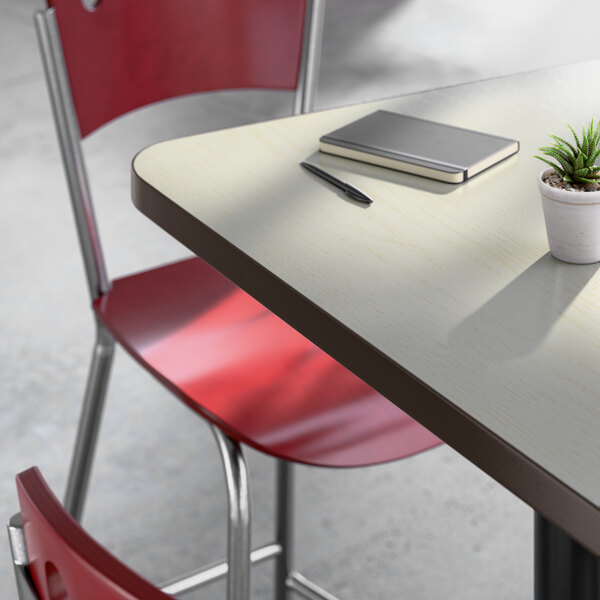 A rectangular laminated table with a white birch and ash finish, paired with a red metal chair and a small potted plant on top.