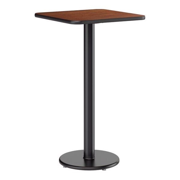 A square bar height table with a reversible walnut and oak laminated top and a black cast iron base.