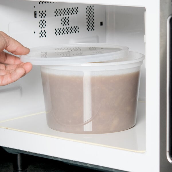 A hand opening a ChoiceHD plastic deli container of food in a microwave.