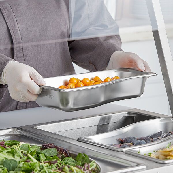 A person in a chef's uniform holding a Vollrath stainless steel tray of food.