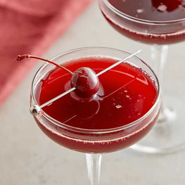 A glass of red liquid with a Les Vergers Boiron Black Cherry puree cocktail with a cherry on top.
