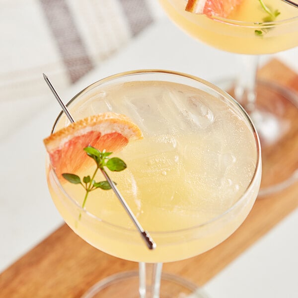 Two glasses of pink grapefruit cocktails with a slice of grapefruit on the rim.