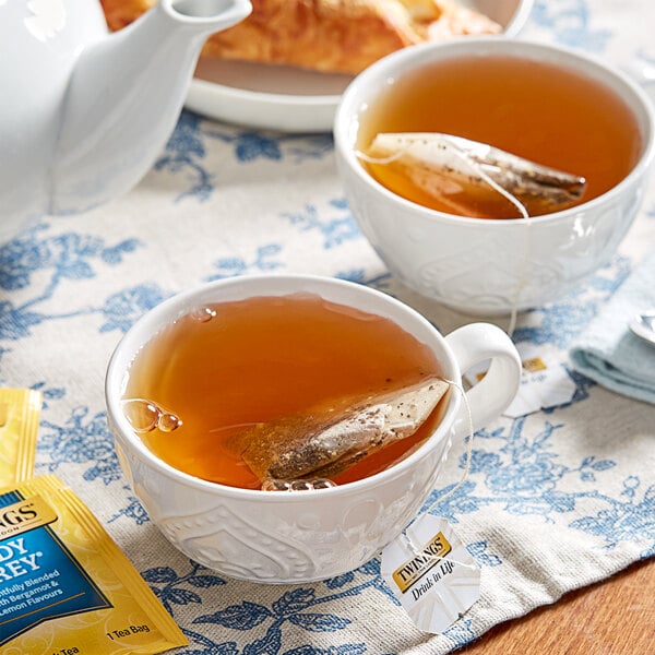 A cup of Twinings Lady Grey Tea with a tea bag in it on a table with a croissant.