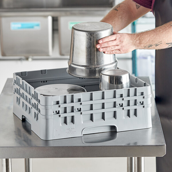 A man using a Cambro soft gray plastic rack to hold metal containers on a counter.