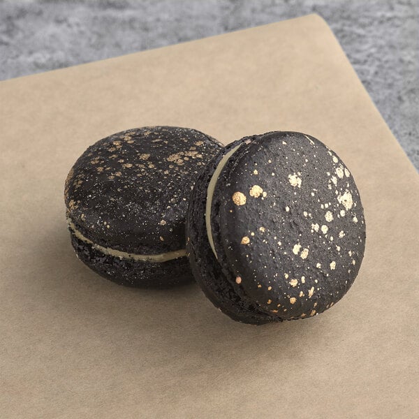 Two black Macaron Centrale Luxe macarons with gold speckled topping.