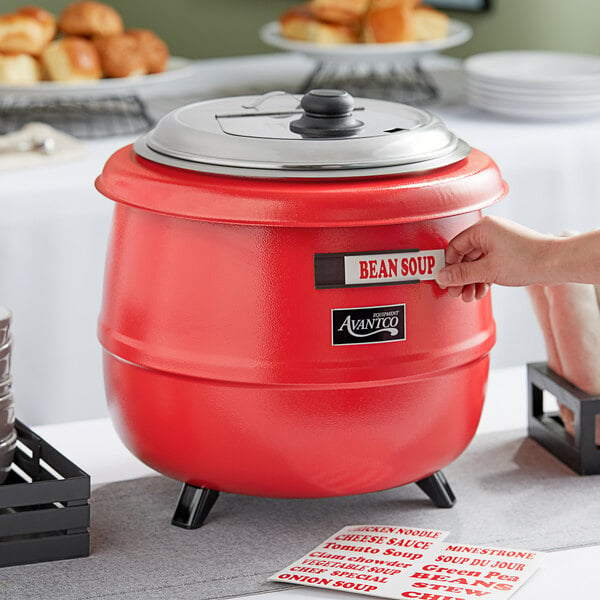 A person holding a red Avantco soup kettle with a lid.