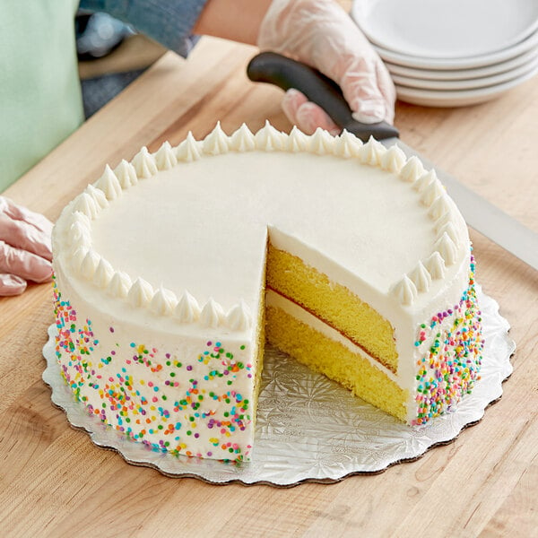 A person's hand holding a knife and cutting a cake on a silver cake circle.