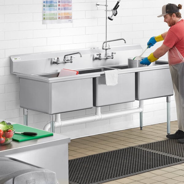 A man washing dishes in a Regency three compartment commercial sink.