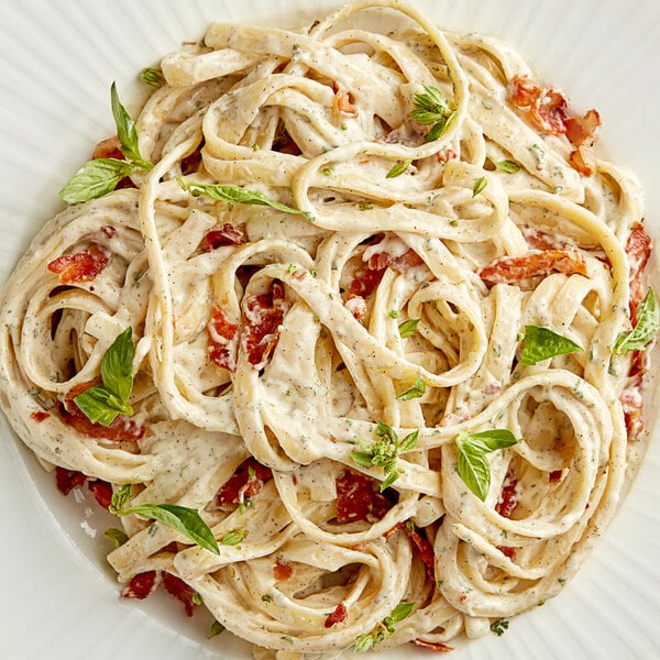 A plate of pasta with sauce and basil next to a container of Regal Italian Seasoning.