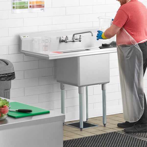 A man in an apron washing a Regency stainless steel commercial sink.