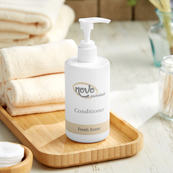 A white bottle of Novo Essentials hotel conditioner on a wooden tray with towels.