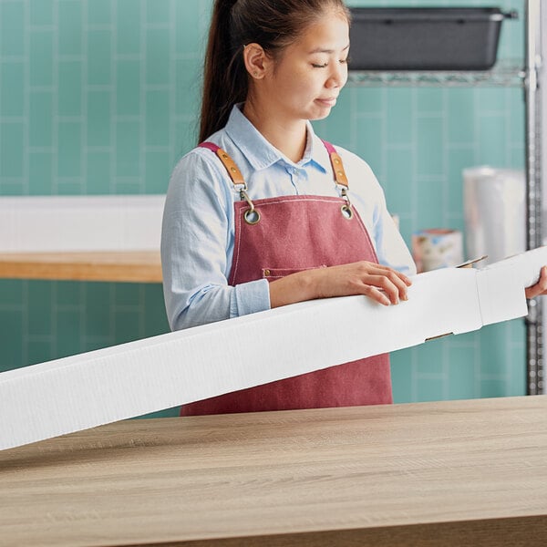 A woman wearing a red apron holding a white Lavex mailing tube box.