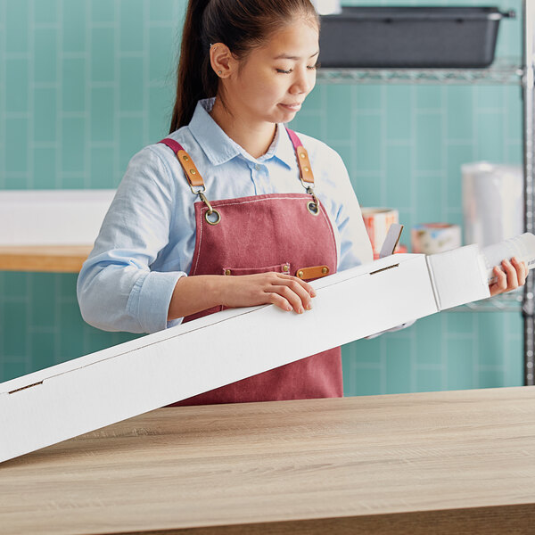 A woman wearing an apron holding a white Lavex mailing tube box.