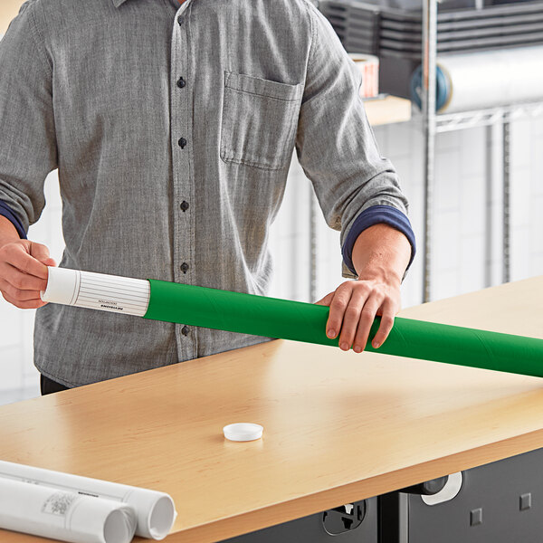 A man holding a green Lavex mailing tube with rolled white paper inside.