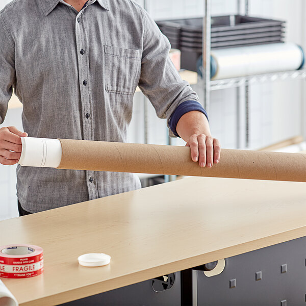 A person holding a Lavex Kraft mailing tube on a table.