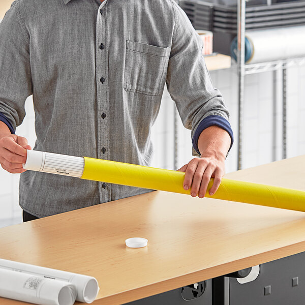 A man holding a yellow Lavex mailing tube on a table.