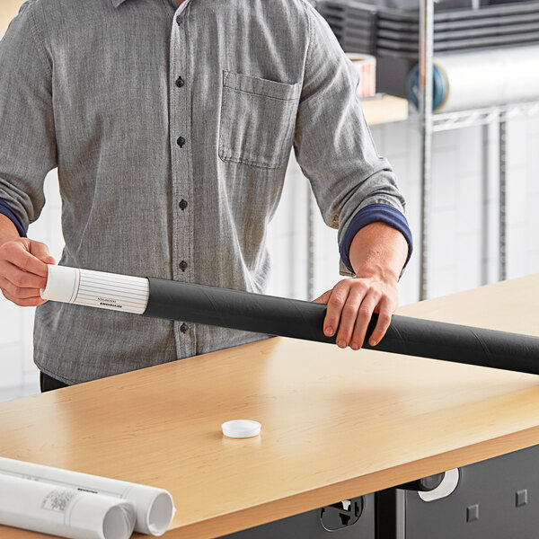 A man holding a rolled up black paper mailing tube.