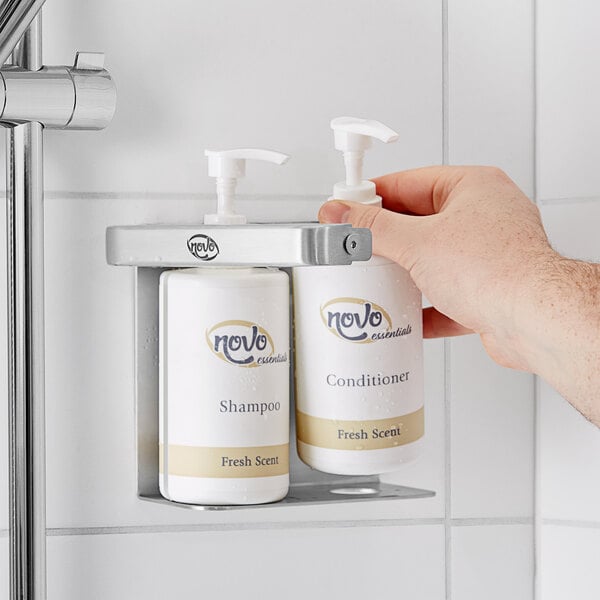 A hand using a Novo by Noble Chemical double bottle bracket to hold bottles of shampoo and conditioner.