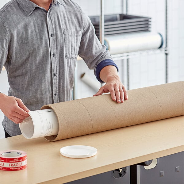 A person using a Lavex heavy-duty mailing tube to hold a roll of brown paper