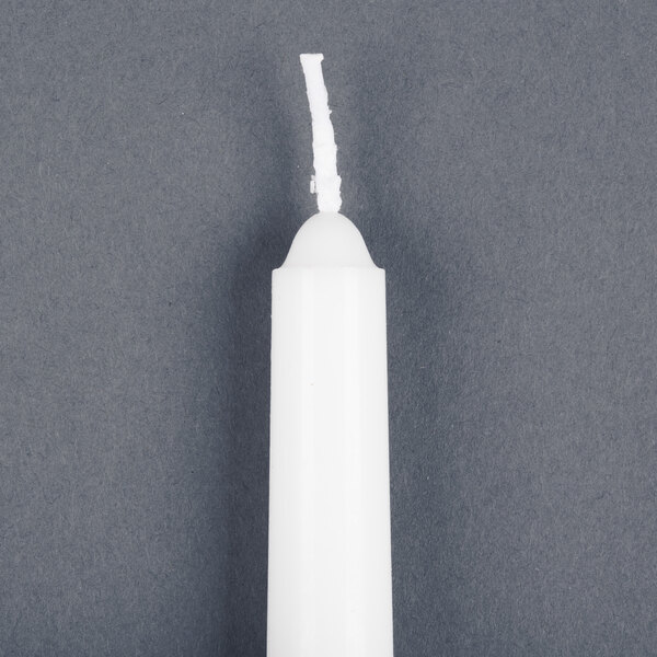 A white Will & Baumer taper candle on a gray surface.