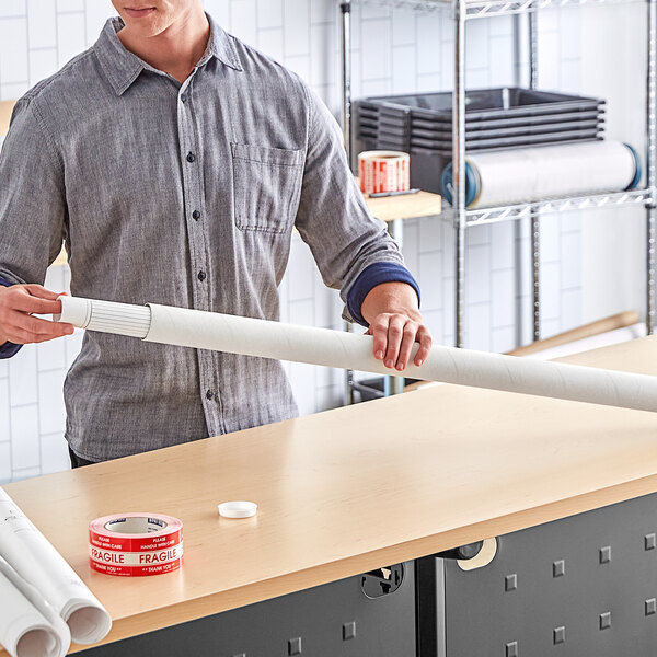 A man holding a Lavex white mailing tube next to a roll of tape.