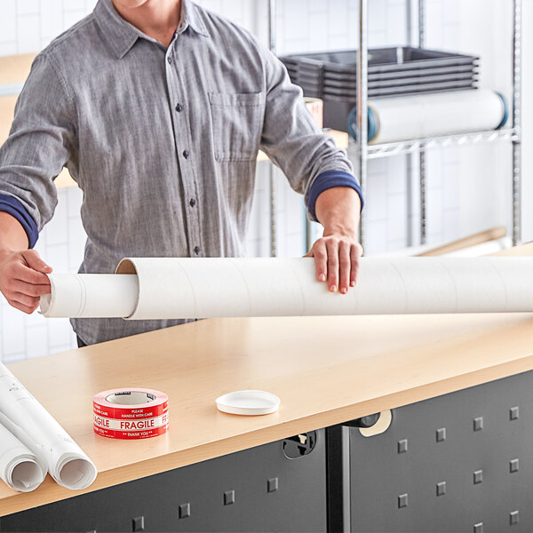 A person holding a Lavex white mailing tube on a table.