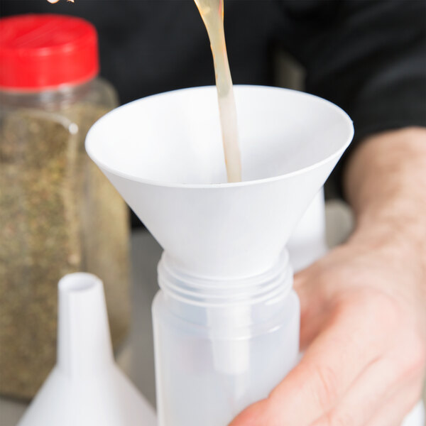 A person pouring liquid into a white Tablecraft plastic funnel.