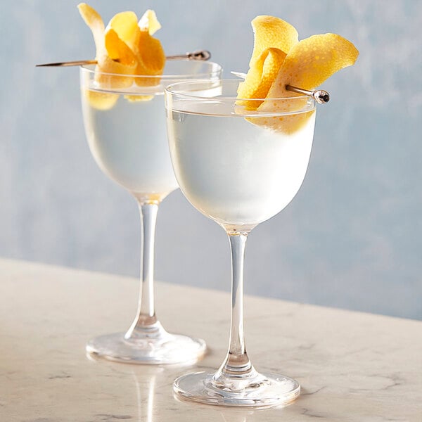 Two Chef & Sommelier Nick and Nora glasses filled with liquid and garnished with lemon peels.