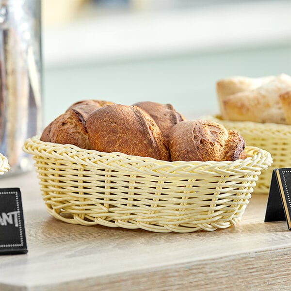 An Acopa oval woven plastic rattan bread basket with bread on a table.