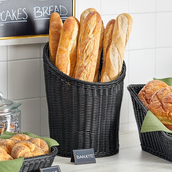 A black woven plastic rattan basket filled with bread on a table in a bakery display.