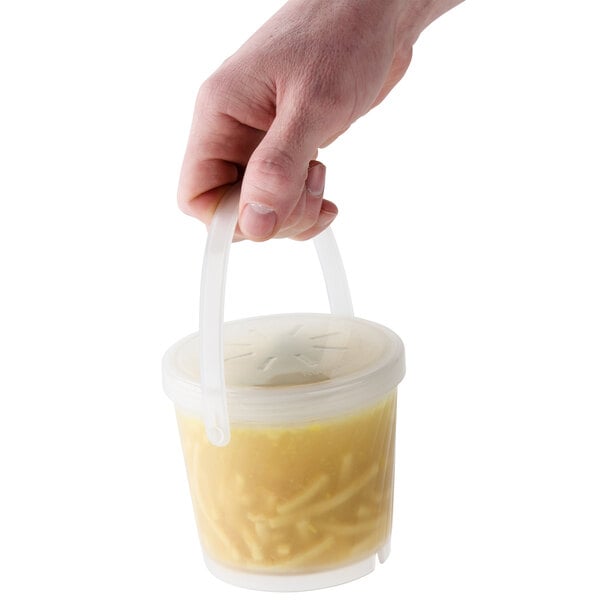 A hand holding a GET clear plastic container of soup.