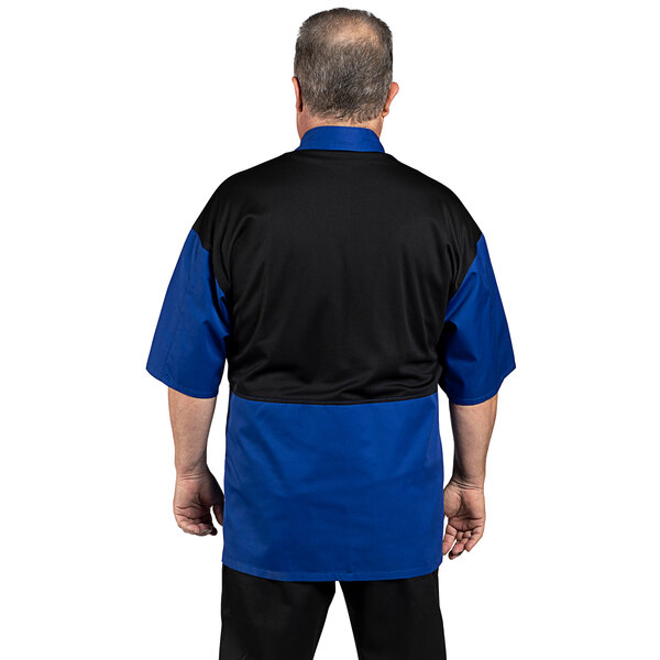 A man wearing a royal blue and black Uncommon Chef short sleeve chef coat with a mesh back.