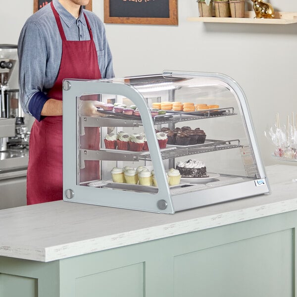 A man standing behind a white Avantco countertop bakery display case filled with cupcakes.