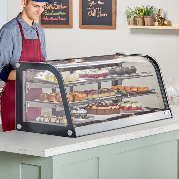 A man standing behind an Avantco countertop bakery display case filled with pastries.