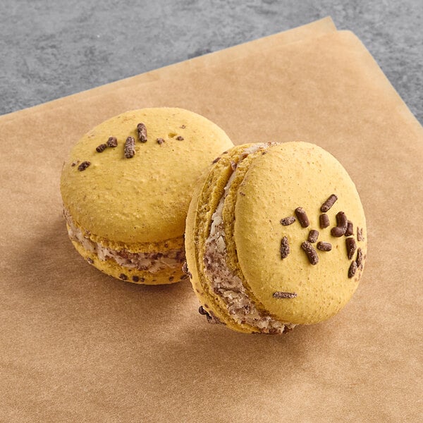 Two yellow Macaron Centrale macarons with chocolate chips on a paper.