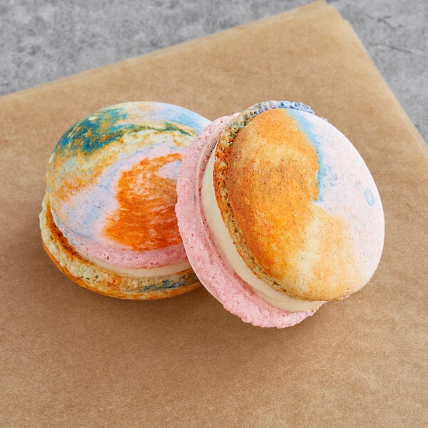 Two Macaron Centrale vegan agave macarons with colorful designs on a brown surface.