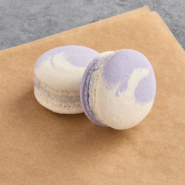 Two purple and white Macaron Centrale vegan butterfly pea macarons on a brown napkin.