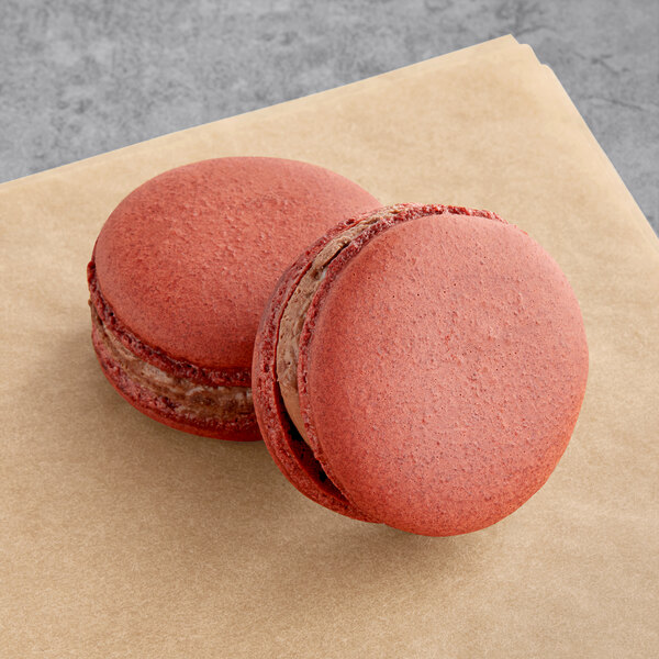 Two red Macaron Centrale vegan red velvet chocolate macarons on a brown napkin.