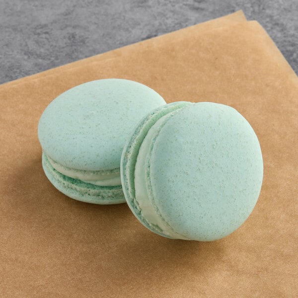 Two blue macarons with white filling on a brown surface.