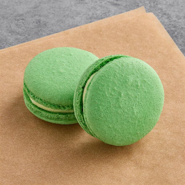 Two green Macaron Centrale vegan apple strawberry macarons on a brown surface.