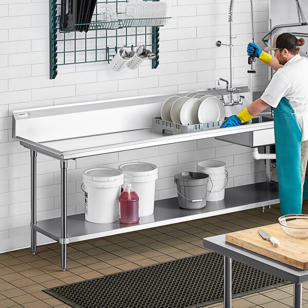 A stainless steel dish table with an undershelf, holding buckets and cleaning supplies, is shown in a commercial kitchen setting.