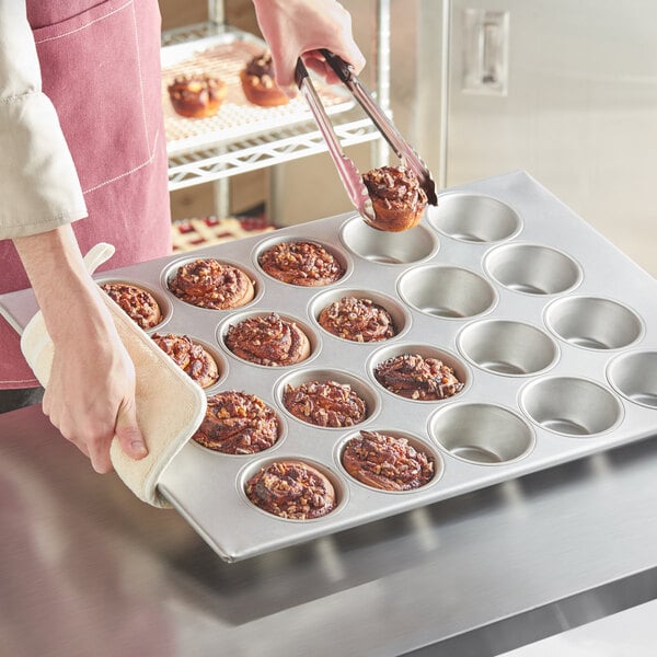 A person holding a Baker's Mark Pecan Roll / Jumbo Muffin Pan filled with muffins.